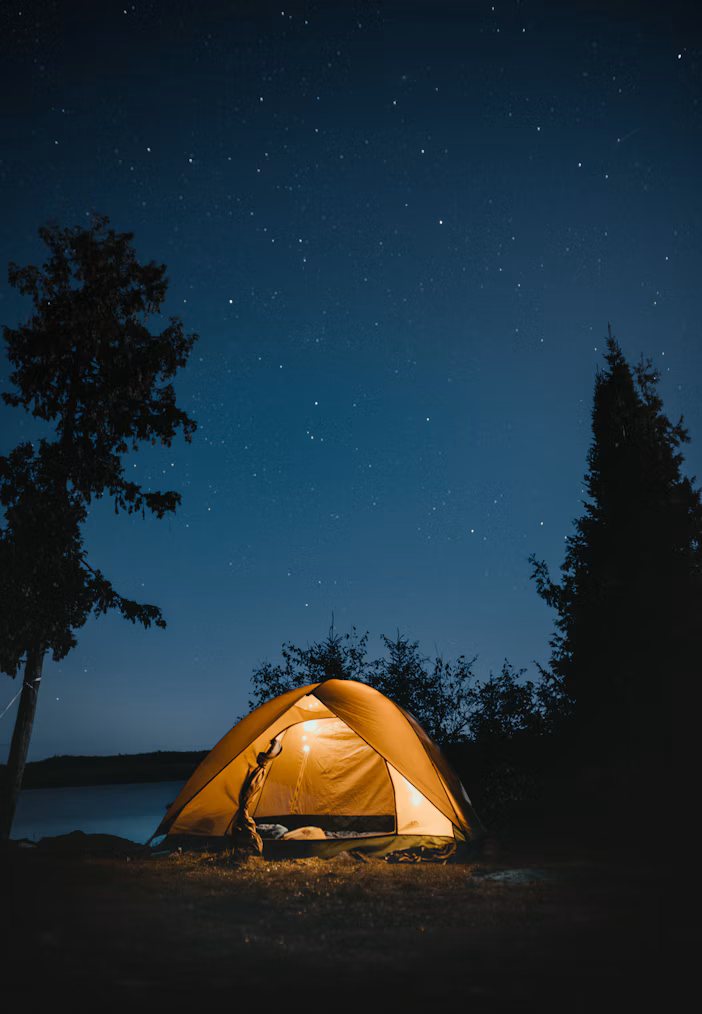 Glowing tent under a starry night sky beside a lake